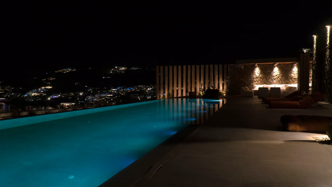 A piscina iluminada à noite, com as luzes da baía ao fundo