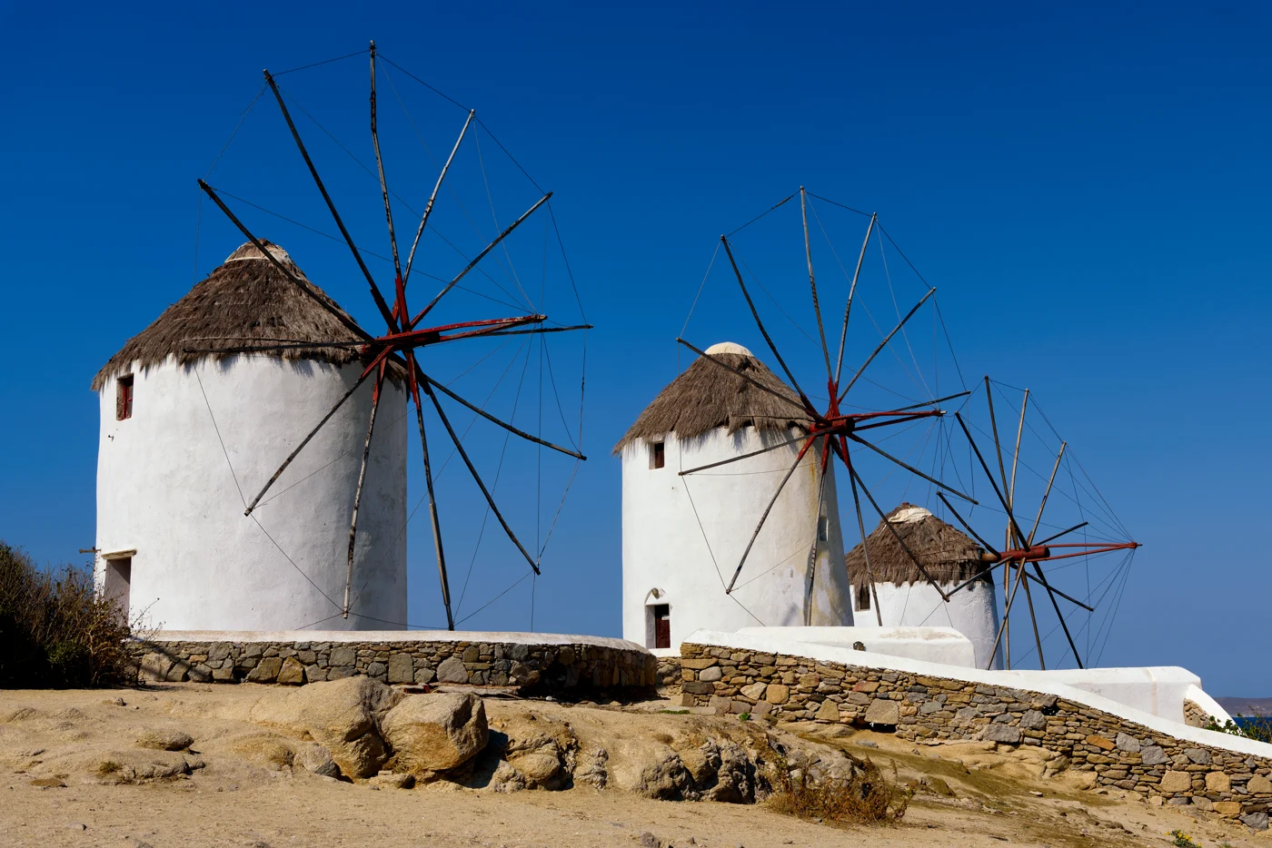 Os moinhos brancos de Mykonos sob o céu azul, com o muro de pedra da colina